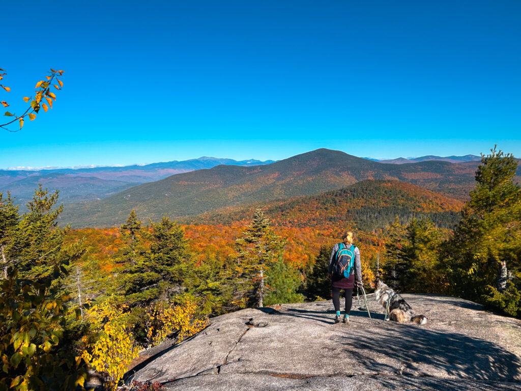 Hiker and dog overlooking the White Mountains from Black Cap Mountain near North Conway, New Hampshire, in fall.